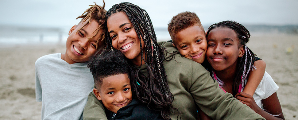 African American mohter with her four foster children smiling on the beach